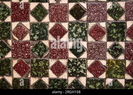 green and maroon red patterned old Italian tile with a unique pattern of squares and diamonds that is very worn from use over time in Italy Europe Stock Photo