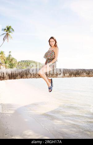 Young woman sitting on palm tree in Ko Samui, Thailand Stock Photo
