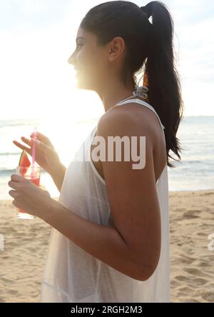 Young woman holding drink on beach Stock Photo