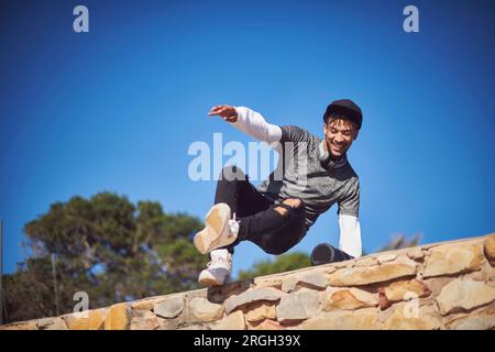 Smiling young man jumping stone wall Stock Photo