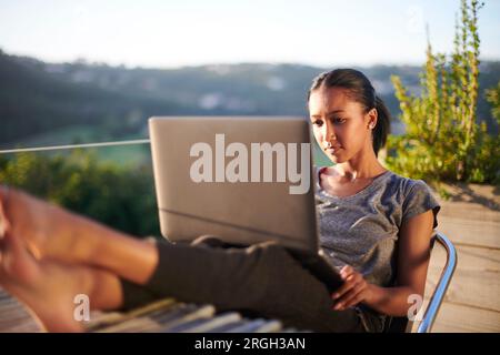 Young woman using laptop on balcony at sunset Stock Photo