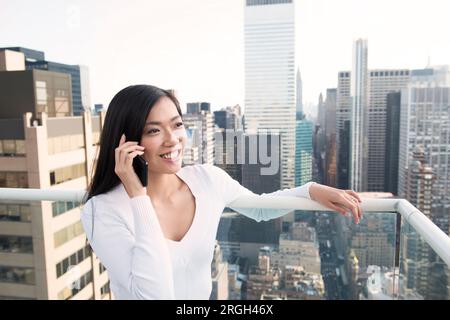 Young woman using smartphone on balcony in New York City Stock Photo