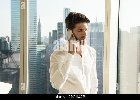 Young man using smartphone by window in New York City Stock Photo