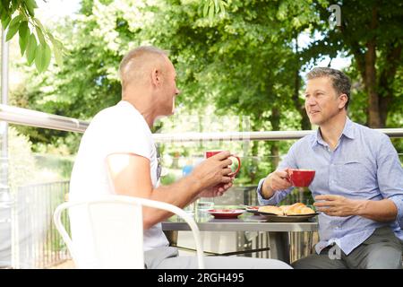 Gay couple having breakfast on balcony Stock Photo