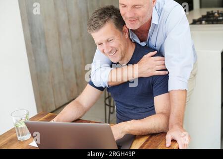 Gay couple embracing while using laptop Stock Photo