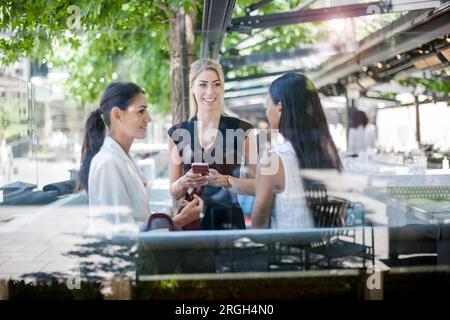 Businesswomen talking on sidewalk behind glass Stock Photo