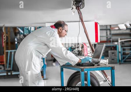Man using laptop by airplane in hangar Stock Photo