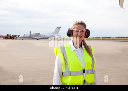Smiling worker wearing ear muffs on airplane runway Stock Photo