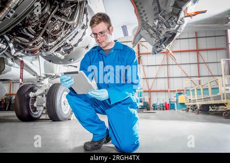 Crouched man using digital table by airplane Stock Photo