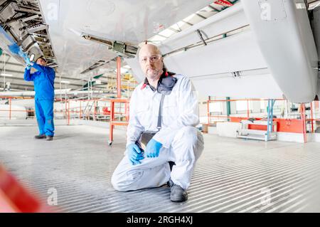 Man holding digital tablet crouched underneath airplane Stock Photo