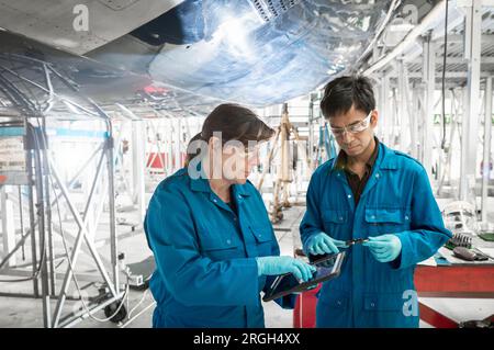 Workers using digital tablet by airplane in hangar Stock Photo