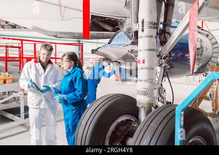Workers using digital tablet by airplane wheels in hangar Stock Photo