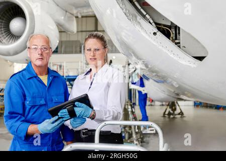Workers using digital tablet by airplane in hangar Stock Photo
