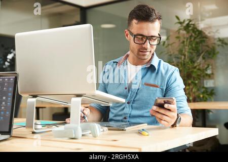 Young man holding smart phone by laptop Stock Photo
