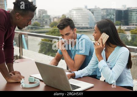 Colleagues using laptop and smart phone on balcony Stock Photo