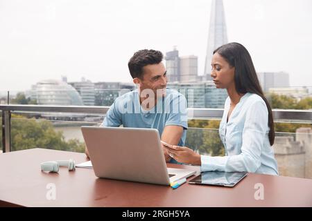 Colleagues using laptop on balcony Stock Photo