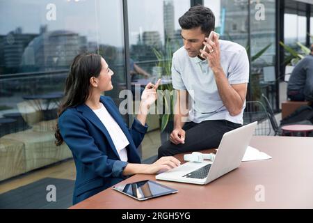 Colleagues using laptop and smart phone on balcony Stock Photo