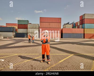 Dock worker in reflective overalls by cargo containers Stock Photo