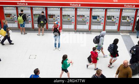 Automated row of ticket machines inside Liverpool Street Station people travellers tourists walking along concourse with luggage bags London UK Stock Photo