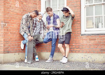 Teenage friends leaning against brick wall Stock Photo