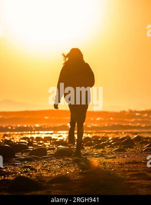 Silhouette of woman walking on beach at sunset Stock Photo