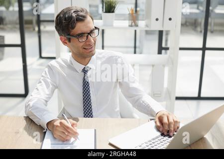 young businessman in a white shirt and tie working in a modern office. Consultant thinks while looking at computer monitor Stock Photo