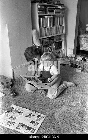 Family life interior home 1970s UK. Mother reading book to baby son sitting on the floor learning to read. Mum spending quality time together with first child. Interior of living room middle class family life 1970s 1975 Southfields, South London UK HOMER SYKES Stock Photo