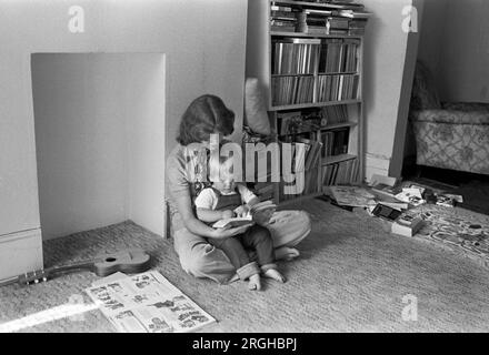 Family life interior home 1970s UK. Mother reading book to baby son sitting on the floor learning to read. Mum spending quality time together with first child. Interior of living room middle class family life 1970s 1975 Southfields, South London UK HOMER SYKES Stock Photo