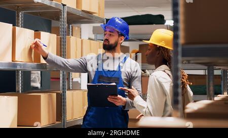 Multiethnic group of people working in storage room with cardboard boxes and stock products, shipping oders. Depot workers checking goods and merchandise in packages, delivery service. Stock Photo