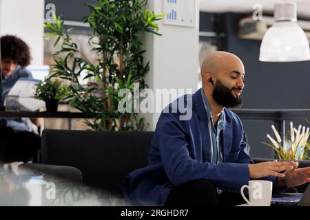 Project manager using video conference app on laptop to manage team remotely while working in business office. Entrepreneur talking in online meeting while sitting on couch at coworking space Stock Photo