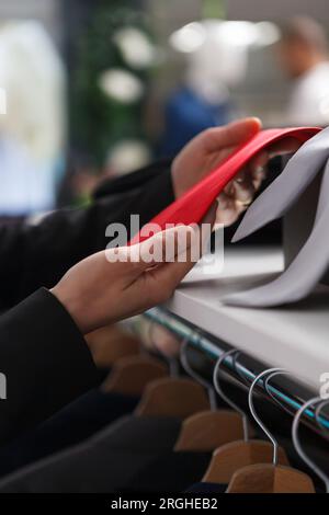 Clothing store woman assistant arms holding red tie while browsing through accessory collection for sale closeup. Boutique seller hands holding merchandise while working in shopping mall Stock Photo