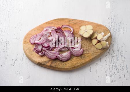Wooden board with chopped red onion and garlic with a knife on a light gray background, top view. Cooking delicious homemade food. Stock Photo