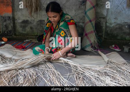 A woman weaves traditional shitol pati (cool mat) at her home in Hailakathi village of Jhalakathi’s Rajapur upazila. Jhalakathi, Bangladesh Stock Photo