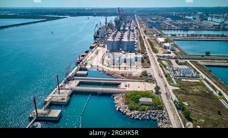 Loading grain into holds of sea cargo vessel in seaport from silos of grain storage. Bunkering of dry cargo ship with grain. Aerial top view. Stock Photo