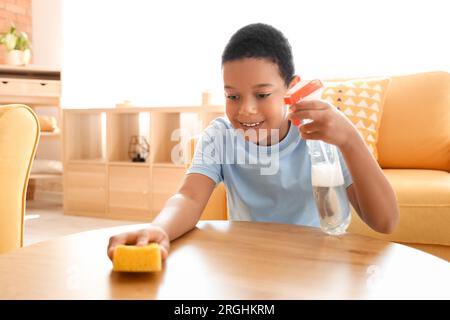 Cute little African-American boy cleaning table with sponge in living room Stock Photo