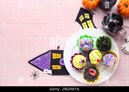 Composition with delicious Halloween cupcakes and paper houses on pink tile background Stock Photo