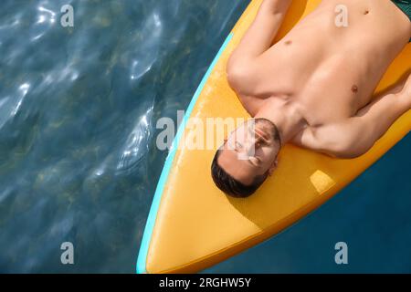 Man lying on SUP board in sea, top view. Space for text Stock Photo