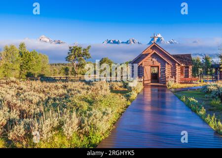 Grand Tetons Mountain Range and the Episcopal Chapel of the Transfiguration at sunrise, bathed in early morning light with fog and low-lying clouds. Stock Photo