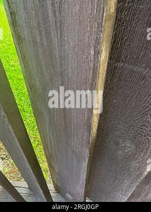 Weathered boards on decorative angled wood weathered  fence are spaced so you can see grass lawn. Text space on board. Stock Photo