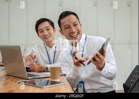 Two cheerful and professional Asian male bankers or financial analysts are working together in the office. Stock Photo