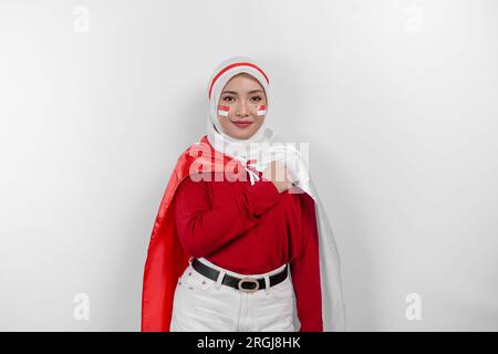 Indonesian muslim woman wearing hijab give salute with proud gesture while holding Indonesia's flag. Indonesia's independence day concept Stock Photo