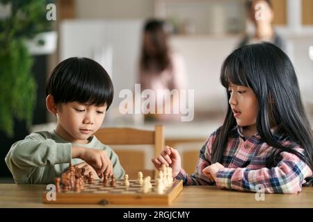 two asian children brother and sister sitting at table at home playing chess Stock Photo