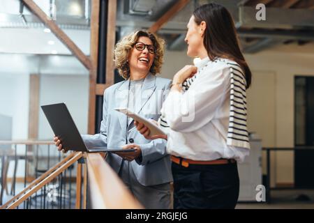 business women smiling as they have a meeting on a balcony. Professional business women discuss their upcoming work and ways to get it done. Women wor Stock Photo