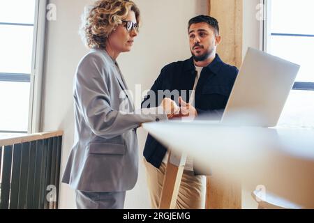 Two business people talking to each other about a project in an office. business professionals using a laptop in a discussion. Colleagues working toge Stock Photo