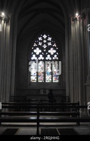 A single figure among the church pews is silhouetted against the stained glass windows Stock Photo