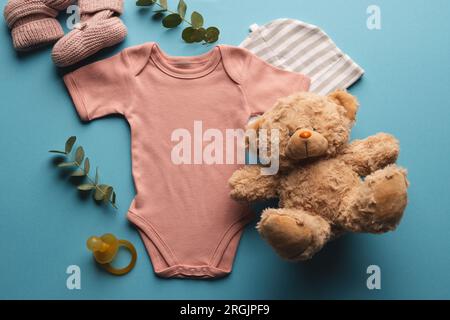 Flat lay of pink baby grow, hat, teddy bear and pink booties with copy space on blue background Stock Photo