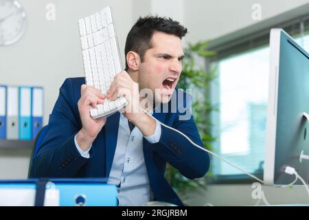 angry businessman breaking keyboard against pc Stock Photo