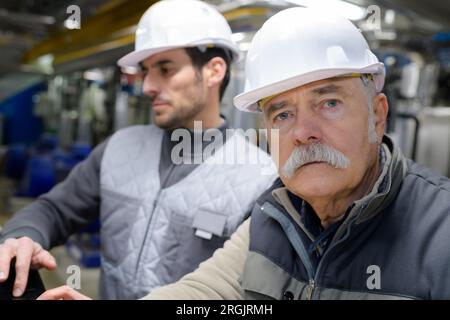 senior worker in safety vest and helmet coworker standing behind Stock Photo