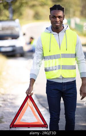 man wearing reflective vest places warning triangle behind breakdown vehicle Stock Photo