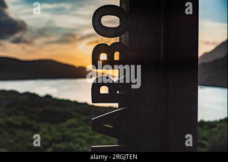 Detail of Killary Harbour sign at sun set with the ocean in background. Killary Fjord sign with the sun setting through the letters and warm colours Stock Photo